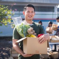 cheerful and smiling asian male volunteer and his colleagues distributing grocery food at community food bank - food stock pictures, royalty-free photos & images