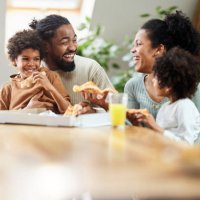 cheerful black family talking while eating pizza for lunch in dining room. - junk food stock pictures, royalty-free photos & images