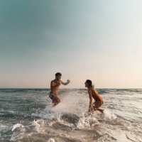 cheerful couple having fun while splashing each other at sea. - travel stock pictures, royalty-free photos & images