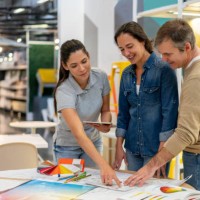 cheerful interior designer holding a tablet and suggesting a color for a home renovation project to customer couple at a furniture store - home decoration stock pictures, royalty-free photos & images