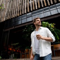 cheerful latin american guy leaving a coffee shop looking away smiling - junk food stock pictures, royalty-free photos & images