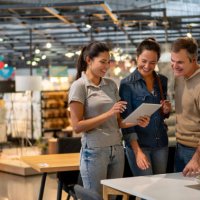 cheerful sales woman showing a design on tablet to mid adult couple looking for furniture at a home store - home decoration stock pictures, royalty-free photos & images