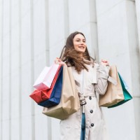 cheerful young lady dancing with colorful shopping bags while standing outdoors. happy dark haired woman enjoying successful shopping during black friday. - fashion stock pictures, royalty-free photos & images