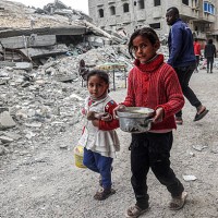 Children walk past the rubble of a collapsed building with a pot of food provided by a charity organisation ahead of the fast-breaking 