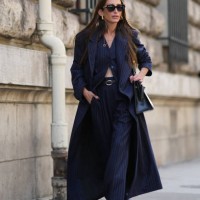 Chloe Harrouche wears sunglasses, a navy blue striped long trench coat, a waistcoat, matching flared suit pants, outside Hermes, during the...