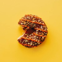 chocolate doughnut with bite on yellow background - junk food stock pictures, royalty-free photos & images