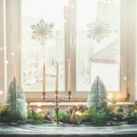 christmas home decoration with candlestick, christmas trees, fir green and pine cones on table with table cloth at window background with hanging snowflakes - home decoration stock pictures, royalty-free photos & images