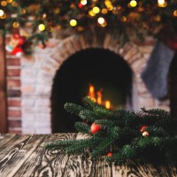 christmas tree branch on a wooden table against the background of a fireplace, place for text, christmas concept, christmas toys and blurry lights - home decoration stock pictures, royalty-free photos & images