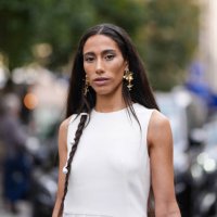 Ciinderella Balthazar wears braided hair with pearl detail, gold earrings, white sleeveless pleaded sheer mesh Akris maxi dress, outside Akris,...