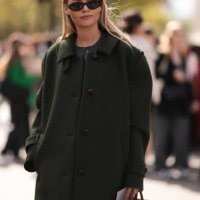 Claire Rose Cliteur is seen wearing a long olive green wool coat, black trousers, red patent shoes, black brown oval sunglasses and a brown leather...