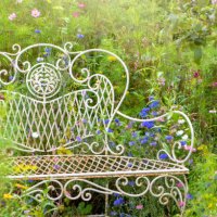 close-up image of a beautiful, vintage style wrought iron garden seat or bench surrounded by summer wild flowers in hazy sunshine - garden decoration stock pictures, royalty-free photos & images