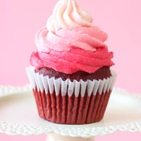 close-up image of individual, homemade, red velvet cupcake in paper cake case on cake stand, decorated with ombre effect pink butter icing piped swirl, pink background, focus on foreground, valentine's day and romance concept