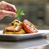 close-up of a chefs hands adding a garnish to a salmon dinner plate. - food stock pictures, royalty-free photos & images