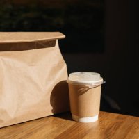 close-up of a drink in a disposable take away cup next to a brown paper bag with take away food on a table - junk food stock pictures, royalty-free photos & images