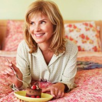 close-up of a mature woman lying on the bed and eating cake - junk food stockfoto's en -beelden