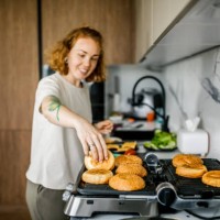 close-up of a woman toasting burger buns on an electric home grill in the kitchen. - junk food stock pictures, royalty-free photos & images