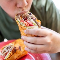 close-up of boy holding and eating wrap sandwich - junk food stock pictures, royalty-free photos & images