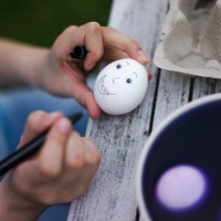 close-up of girl painting face on easter egg on garden table - garden decoration stock-fotos und bilder