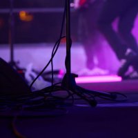 close-up of low section of a microphone stand with musicians playing on the background on a lighted stage during a music concert at night - concert stock pictures, royalty-free photos & images