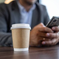 close-up of takeaway coffee on desk with businessman using smartphone - junk food stock pictures, royalty-free photos & images