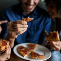 close-up of tattooed man with friends holding pizza slice - junk food stock pictures, royalty-free photos & images