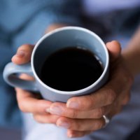 close-up of woman holding coffee cup at home - coffee stockfoto's en -beelden