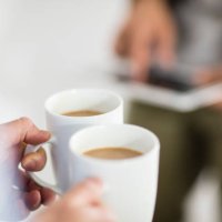 close-up of woman holding coffee cups while man using tablet in office - coffee stockfoto's en -beelden