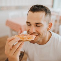 close-up of young man with eyes closed eating pizza while sitting in restaurant - junk food stock pictures, royalty-free photos & images