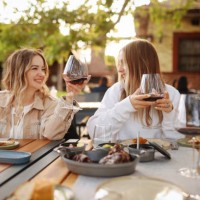 close-up portrait of two female friends in strict suits laughing drinking wine on the terrace outside at summer street cafe - food stock pictures, royalty-free photos & images