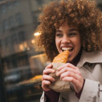 close up beautiful young woman eating croissant outdoors - junk food stock pictures, royalty-free photos & images