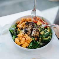 close up, high angle shot of young woman enjoying multi-coloured healthy fruit, vegetables with grilled chicken salad bowl with balanced nutrition in cafe, with a glass of water by the side. healthy eating lifestyle. people, 