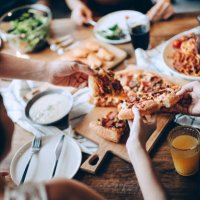 close up of a young group of friends passing and serving food while enjoying together. they are having fun, chatting and feasting on food and drinks at dinner party - food stock pictures, royalty-free photos & images