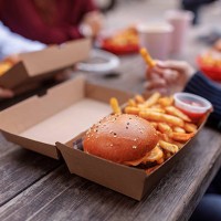 close up of burger in box on a table with teenagers around it - junk food stock pictures, royalty-free photos & images