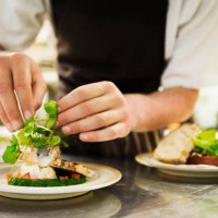 close up of chef in kitchen adding salad garnish to a plate with grilled fish. - food stock pictures, royalty-free photos & images