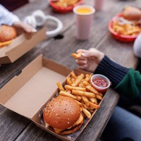 close up of hand holding french fries, there is a box with burger on a table - junk food stock pictures, royalty-free photos & images