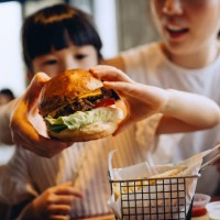 close up of lovely little asian girl and her mother dining out in restaurant, sharing burger and french fries together. asian family enjoying a happy meal. family eating out lifestyle - junk food stock pictures, royalty-free 