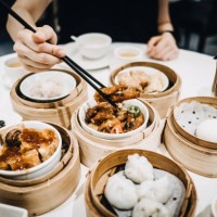 close up of woman enjoying chinese tea and a variety of freshly made dim sum with chopsticks in restaurant - junk food stockfoto's en -beelden