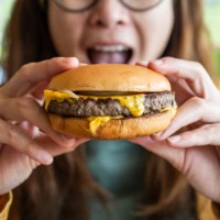close up of woman opened her mouth to eat a classic beef cheeseburger. - junk food stock pictures, royalty-free photos & images