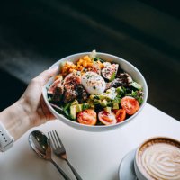 close up of woman's hand holding a bowl of fresh beef cobb salad, serving on the dining table. ready to enjoy her healthy and nutritious lunch with coffee. maintaining a healthy and well-balanced diet. healthy eating lifestyl