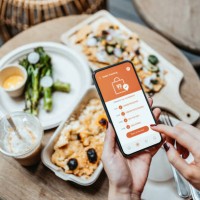 close up of woman's hand ordering home delivery takeaway food with mobile app on smartphone, tracking status and confirming food order. enjoying nachos, baked mac and cheese and baby broccoli in the balcony at home. technolog