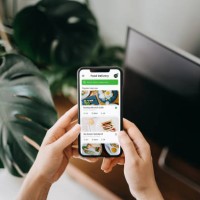 close up of young asian woman's hand using meal delivery service and ordering food online with smartphone in the living room at home, against green potted plants - junk food stock pictures, royalty-free photos & images