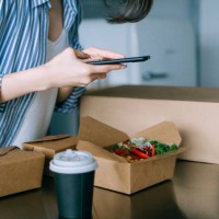 close up of young asian woman standing by the kitchen counter, taking a photo of delicious home delivery takeaway lunch box of fresh healthy salad with smartphone, sharing on social media before eating it. eating at home conc