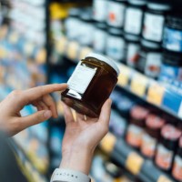 close up of young woman grocery shopping in a supermarket. standing by the aisle, holding a bottle of marmalade, reading the nutritional label and checking ingredients at the back - food fotografías e imágenes de stock