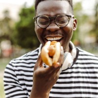 close up portrait of young man eating hot dog outdoors - junk food stock pictures, royalty-free photos & images
