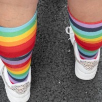 Close up rear view of legs and feet of person wearing knee high socks with colorful repeating rainbow rings design and white athletic shoes and who...