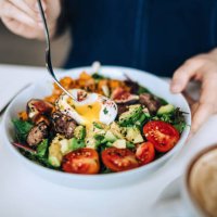 close up shot of a woman eating a dish of fresh beef cobb salad with a soft boiled egg and coffee at a cafe table. enjoying her healthy and nutritious lunch. maintaining a healthy and well-balanced diet. the concept of health
