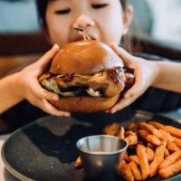 close up shot of lovely little asian girl enjoying eating a big burger with sweet potato fries in a restaurant. eating out lifestyle - junk food stock pictures, royalty-free photos & images