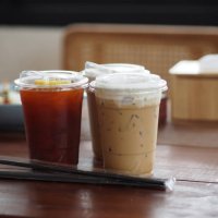 close up view of ice cubes in cold brewed coffee cappuccino in plastic cup put on bamboo wooden desk blurred background, drink beverage - junk food stock pictures, royalty-free photos & images