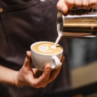 close up view of young woman preparing a coffee by drawing a flower with milk - coffee stock pictures, royalty-free photos & images