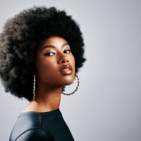 closeup of a young, stylish, and edgy black woman standing or posing against a grey studio background alone. one confident, trendy and sassy female with an afro looking powerful and wearing makeup - fashion stock pictures, ro